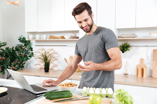 Man with laptop preparing a nutritions meal holding and gazing at an egg